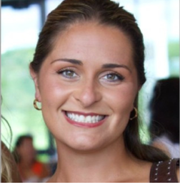 A woman with light brown hair pulled back, wearing gold hoop earrings, smiles at the camera. The background is blurred with hints of greenery and people.