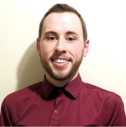 A person with short hair and a trimmed beard is smiling at the camera, wearing a burgundy button-up shirt against a plain light-colored background.