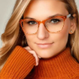 A woman with long blonde hair wearing clear tortoiseshell glasses and an orange turtleneck sweater rests her chin on her hand.