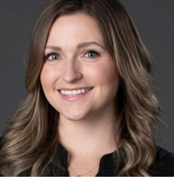 A woman with long, wavy light brown hair and a black top smiles in front of a dark gray background.