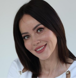 Woman with straight dark hair wearing a white top, smiling at the camera against a plain light background.