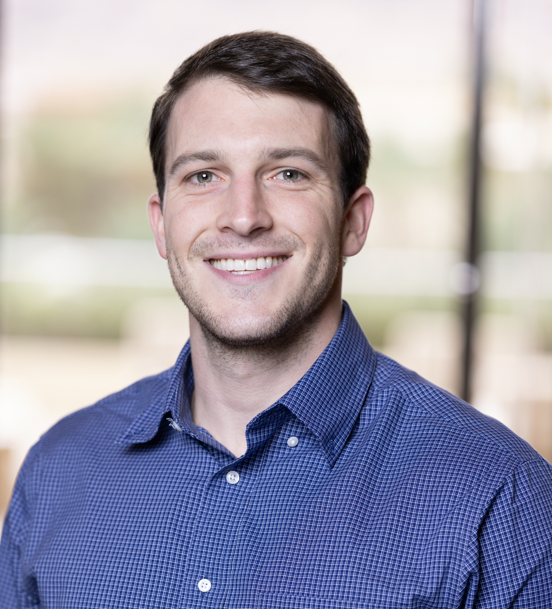 A smiling man wearing a blue button-down shirt.