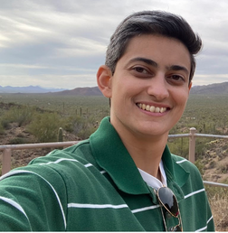 Person taking a selfie outdoors, wearing a green striped shirt and sunglasses, with a desert landscape and mountains in the background.