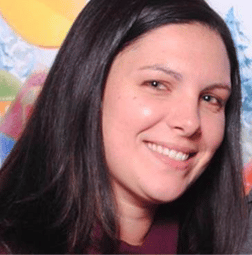 A woman with long dark hair smiles at the camera, with a colorful, blurred background behind her.